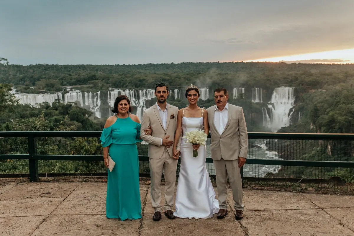 Oswaldo, Gustavo, Amanda e Maria Inês, a família Vicenzi, vestidos de festa, sorrindo juntos diante das Cataratas do Iguaçu.